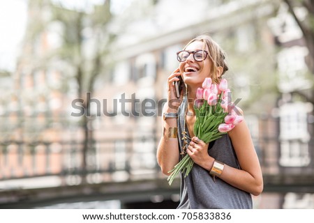Young woman talking with smart phone sitting with flowers near the water channel in Amsterdam old city
