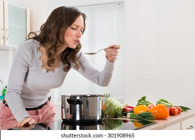 Young Woman Tasting Food With Spoon In Kitchen