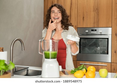 Young woman tasting healthy detox juice made with the blender at home. Fit girl tasting green juice blending with fresh fruits and vegetables in kitchen. Happy smiling girl preparing fruit smoothie. - Powered by Shutterstock