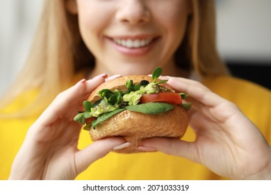 Young woman with tasty vegan burger at home, closeup