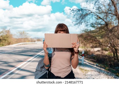 Young woman with tattoed hand holding a cardboard sign with mock up and cover her face. Copy space. Outdoor. The concept of local traveling and hitchhiking.