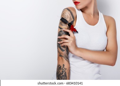 Young woman tattooist with a tattoo-machine in her hand on white background