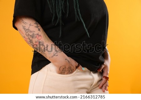 Young woman with tattoos on arm against yellow background, closeup