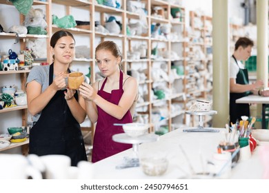 Young woman teacher in apron examines ceramic cup made by teenage girl student.. - Powered by Shutterstock