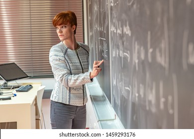 Young Woman Teacher In College. Instruction In A University Classroom. Blackboard Described By Chalk. Projection From The Data Projector