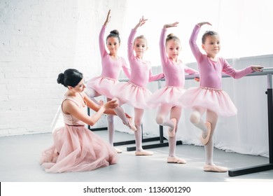young woman teaching adorable children dancing in ballet school 