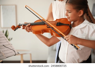 Young woman teaching little girl to play violin indoors - Powered by Shutterstock