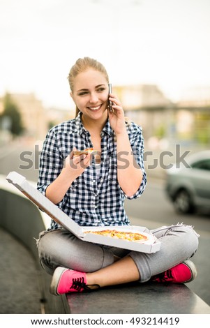Young woman - teenage girl eating pizza in street and calling phone