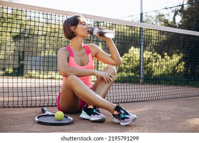 Young woman tennis player sitting on the court and drinking water - Powered by Shutterstock