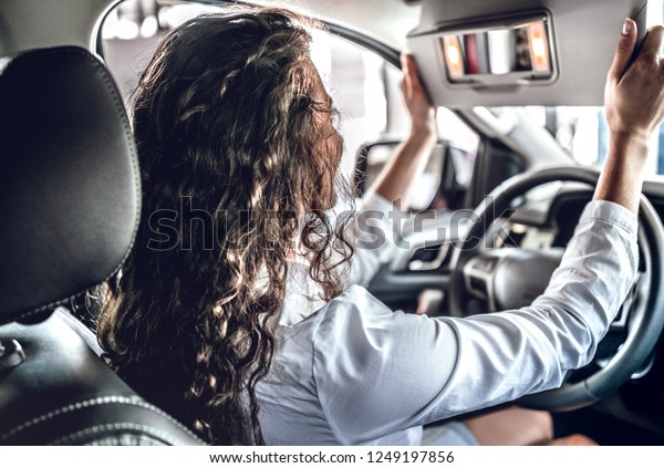 Young woman testing new car in salon. Woman\
looking on rearview\
mirror