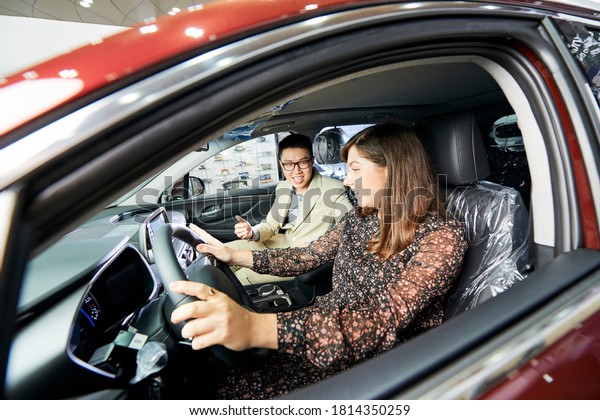 Young woman testing the new car\
together with salesman while they sitting in salon of the\
car