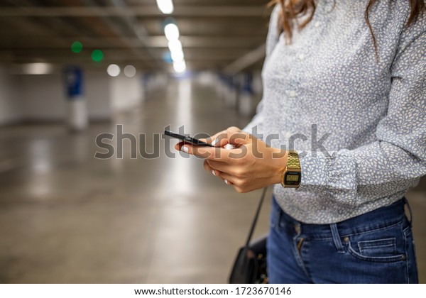 A young woman texting on the\
phone at a parking lot. Texting in the subway parking lot. Photo of\
Businesswoman with smart phone at night time in parking\
garage