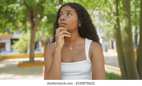 Young woman thinking in an urban park, thoughtfully gazing upwards surrounded by trees and cityscape in the background - Powered by Shutterstock