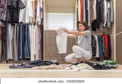 Young Woman Throwing Clothes In Walk In Closet. Mess In Wardrobe And Dressing Room