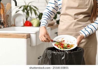 Young woman throwing organic food into trash bin in kitchen, closeup. Waste recycling concept - Powered by Shutterstock