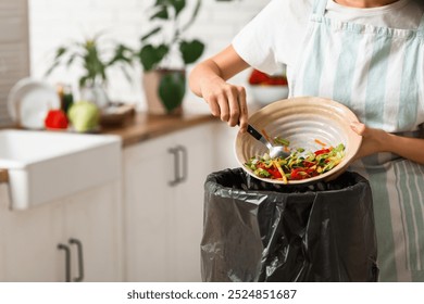 Young woman throwing organic food into trash bin in kitchen, closeup. Waste recycling concept - Powered by Shutterstock