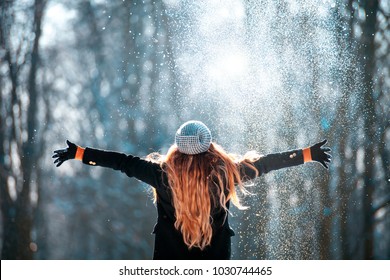 Young woman throwing snow in the air at sunny winter day, back view
