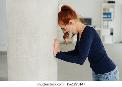 Young Woman Throwing A Temper Tantrum At Work In The Office Screaming And Banging Her Head Against A Pillar, With Lateral Copy Space