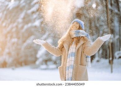 A young woman throws out snow. Portrait of a happy woman playing with snow on a sunny winter day. A walk through the winter forest. Concept of fun, relaxation. - Powered by Shutterstock