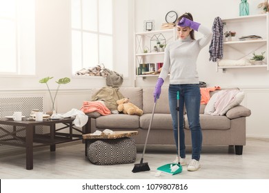 Young Woman Tired Of Spring Cleaning House, Sweeping Floor With Broom And Scoop In Messy Room, Copy Space