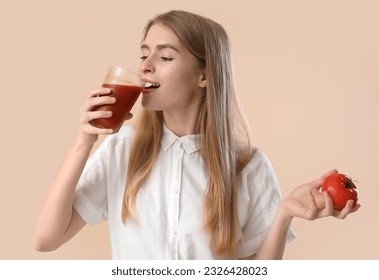 Young woman with tomato drinking vegetable juice on beige background