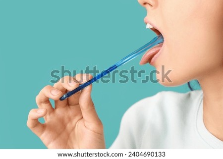 Young woman with tongue scraper on blue background