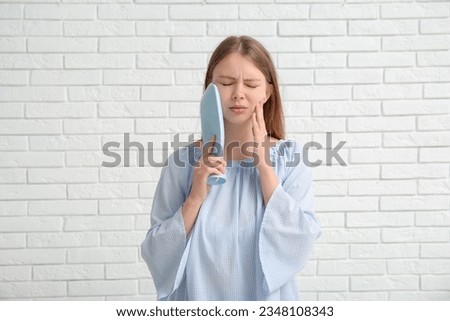 Young woman with tooth ache holding cold compress on white brick background