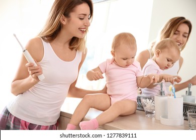 Young woman with toothbrush and daughter near mirror in bathroom
