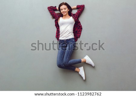 Young woman top view isolated on grey lying on floor relaxed looking amera smiling happy hands beside head