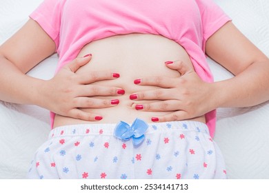 A young woman touches her abdomen while lying on the bed; abdominal pain during menstruation is very common. - Powered by Shutterstock