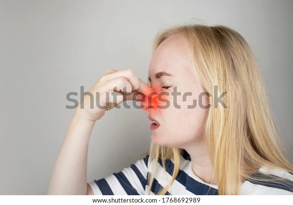 A young woman touches her nose,\
which is very painful. Medical care concept for difficulty\
breathing, clogged nasal passages and flu, colds or\
coronavirus