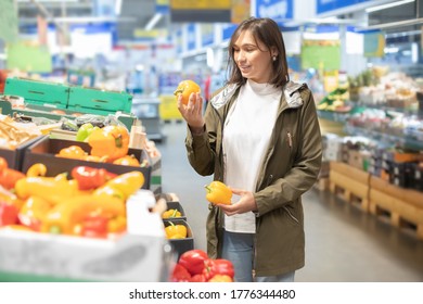 Young woman touches peppers to determine its quality in the supermarket