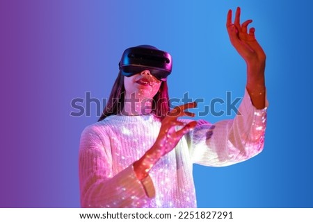 Young woman touching air and wearing virtual reality headset. Future digital vr technology and entertainment. Dark colorful background pink with blue