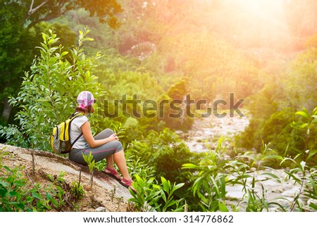 Young woman tourist with backpack relaxing on top of the mountain and enjoying beatiful sunset.
 Ecotourism concept image, with happy female hiker.