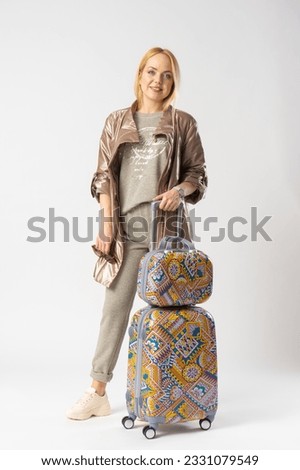 Young woman tourist in casual clothes, with a large multi-colored travel suitcase for travel. Model posing in the studio on a white background.