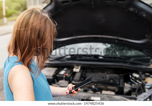 Young woman\
tourist driver standing by the road by the car with the hood open\
dead engine broken automobile malfunction repair in a summer day\
making a mobile phone call for\
help