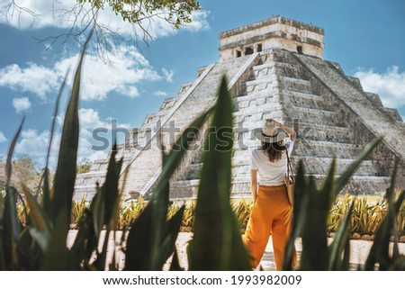 A young woman tourist in a hat stands against the background of the pyramid of Kukulcan in the ancient Mexican city of Chichen Itza. Travel concept.Mayan pyramids in Yucatan, Mexico 