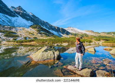 Young woman tourist looking at mountains and standing on a rock in alpine lake, Gasienicowa valley, High Tatra Mountains, Poland 