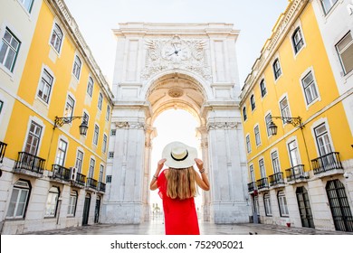 Young woman tourist in red dress standing back in front of the famous triumphal arch in Lisbon city center in Portugal