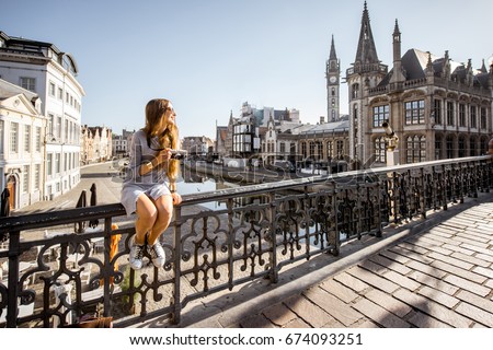 Young woman tourist sitting on the bridge in the old town of Gent city durnig the sunrise in Belgium