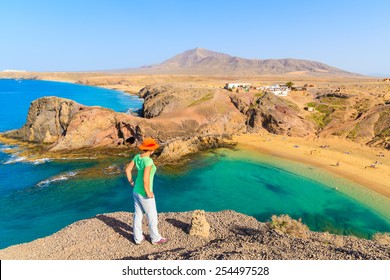 Young Woman Tourist Standing On Cliff Looking At Papagayo Beach, Lanzarote, Canary Islands, Spain