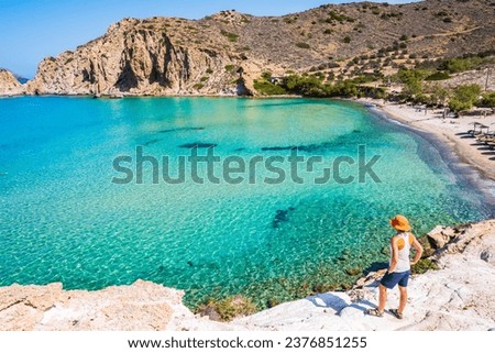 Young woman tourist standing on rock and looking at amazing Plathiena beach, Milos island, Cyclades, Greece