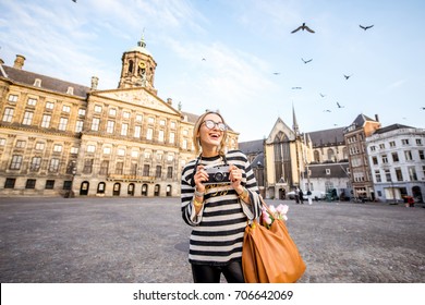 Young woman tourist standing with photo camera on the Dam central square during the morning in the old town of Amsterdam city