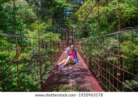 Young woman - tourist standing in a red suspension bridges in Santa Elena Cloud Forest Reserve, in Monteverde, Costa Rica. Foggy rainforest in the mountains. Central America.