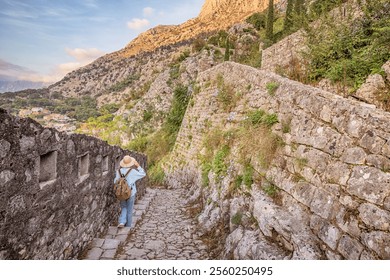 Young woman tourist walking up cobblestone path in historic town of Kotor, Montenegro, exploring ancient fort on a mountain - Powered by Shutterstock