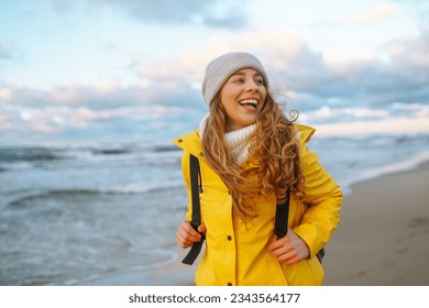 Una joven turista con un abrigo amarillo camina a lo largo de la orilla del mar, disfruta del paisaje marino al atardecer. Viajes, concepto de turismo. Estilo de vida activo.