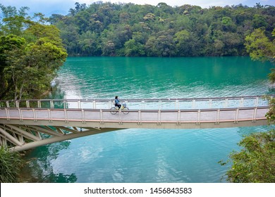 Young woman tourists riding bicycle across the white bridge at Sun moon lake in Nantou, Taiwan