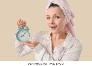 Young woman in towel with alarm clock after shower on beige background - Powered by Shutterstock