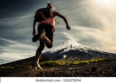 Young woman, trail running athlete runs on the trail with loose ground and volcano on the background
