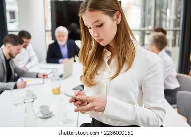 Young woman as a trainee in a business meeting reads SMS or checks news on the smartphone - Powered by Shutterstock